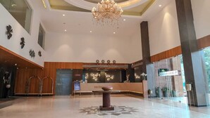 Et hotellobby med lysekrone, receptionsdisk og et stort vindue.