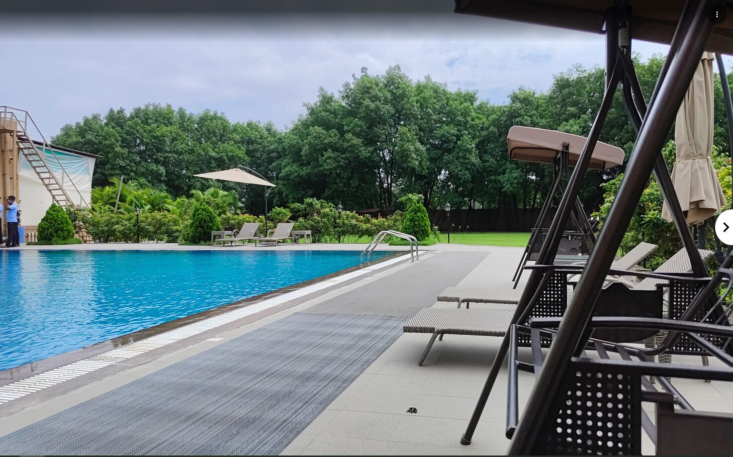 Una piscina con sillas de descanso, un área de estar cubierta y vistas a árboles.
