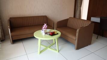 A room with a brown sofa and a small round table with a vase and fruit.