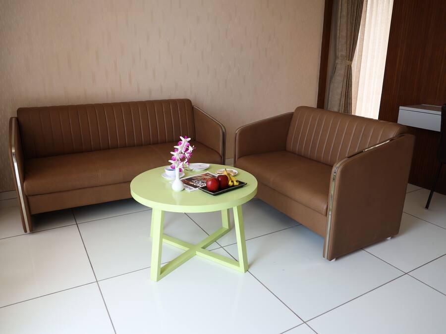 Una habitación con un sofá marrón y una pequeña mesa redonda con un florero y fruta.