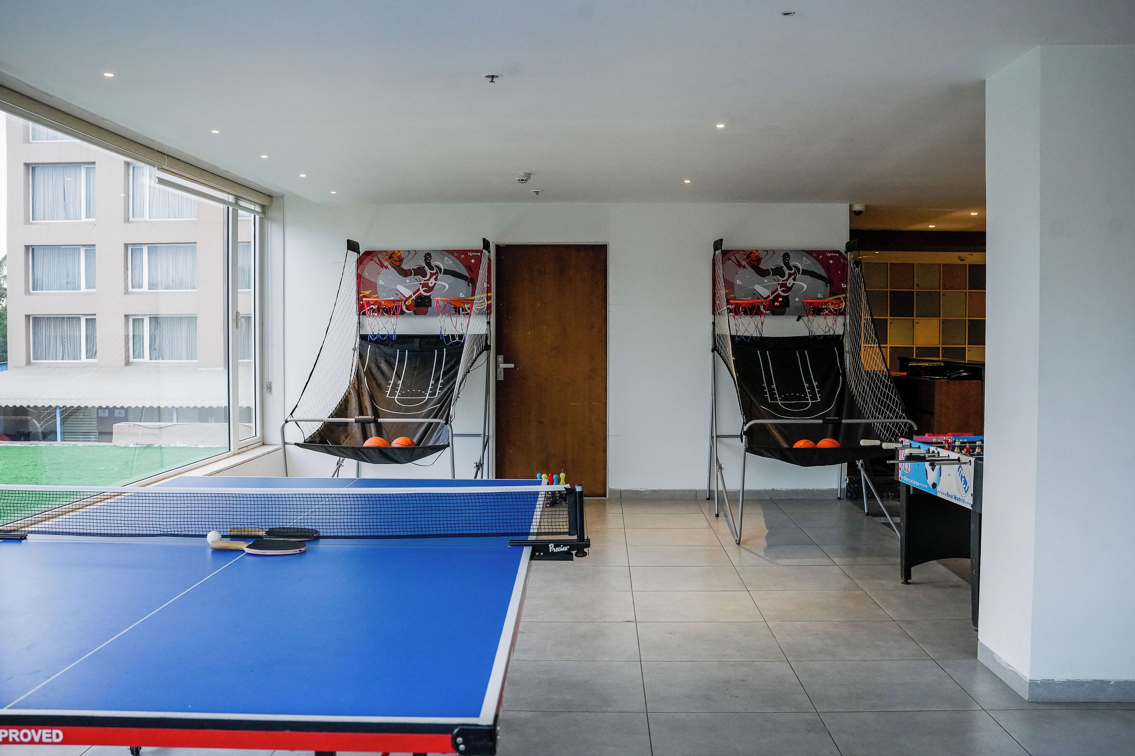 A room with a ping pong table, two foosball tables, and a tennis table.
