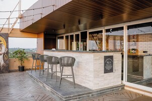 Una zona de bar con taburetes, un cartel que dice 'Sea Breeze' y vistas de la ciudad a través de amplias ventanas.