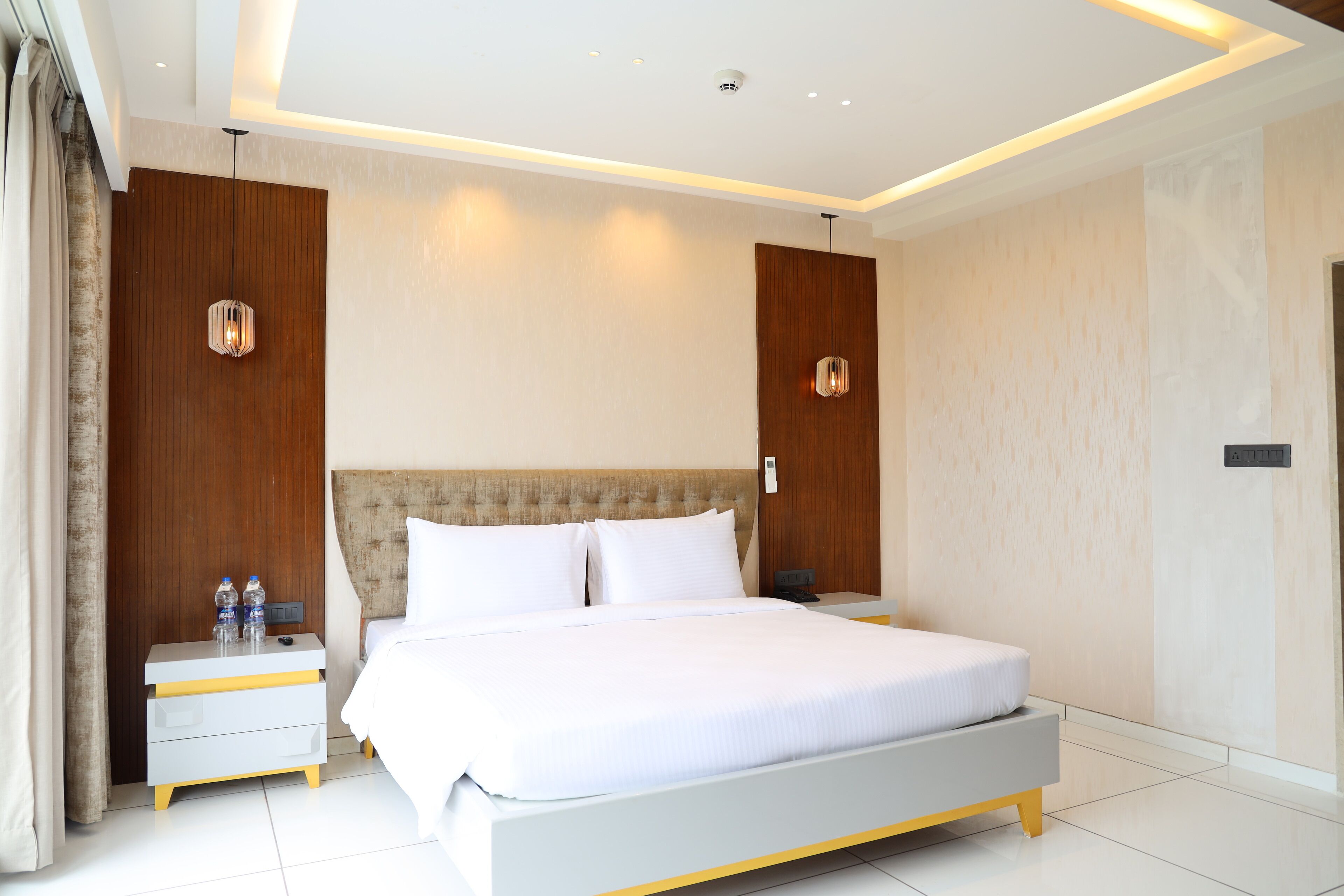 Una habitación de hotel moderna con una cama grande, mesitas de noche y una lámpara en el techo.