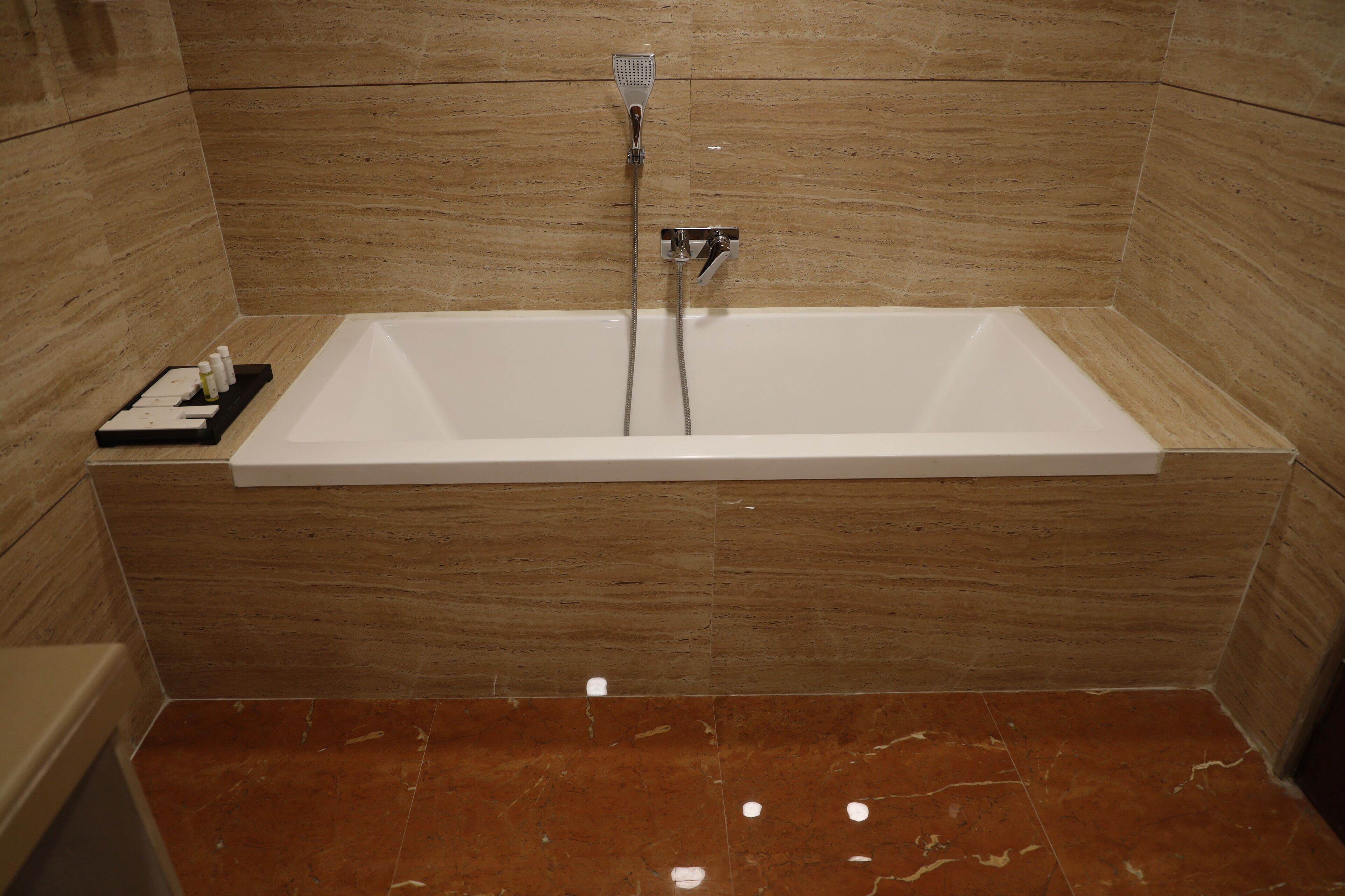 A modern bathroom with a rectangular bathtub, wooden wall panels, and a marble floor.