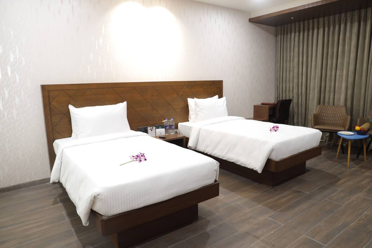A hotel room with two beds, a desk, a chair, and a small table with fruit.