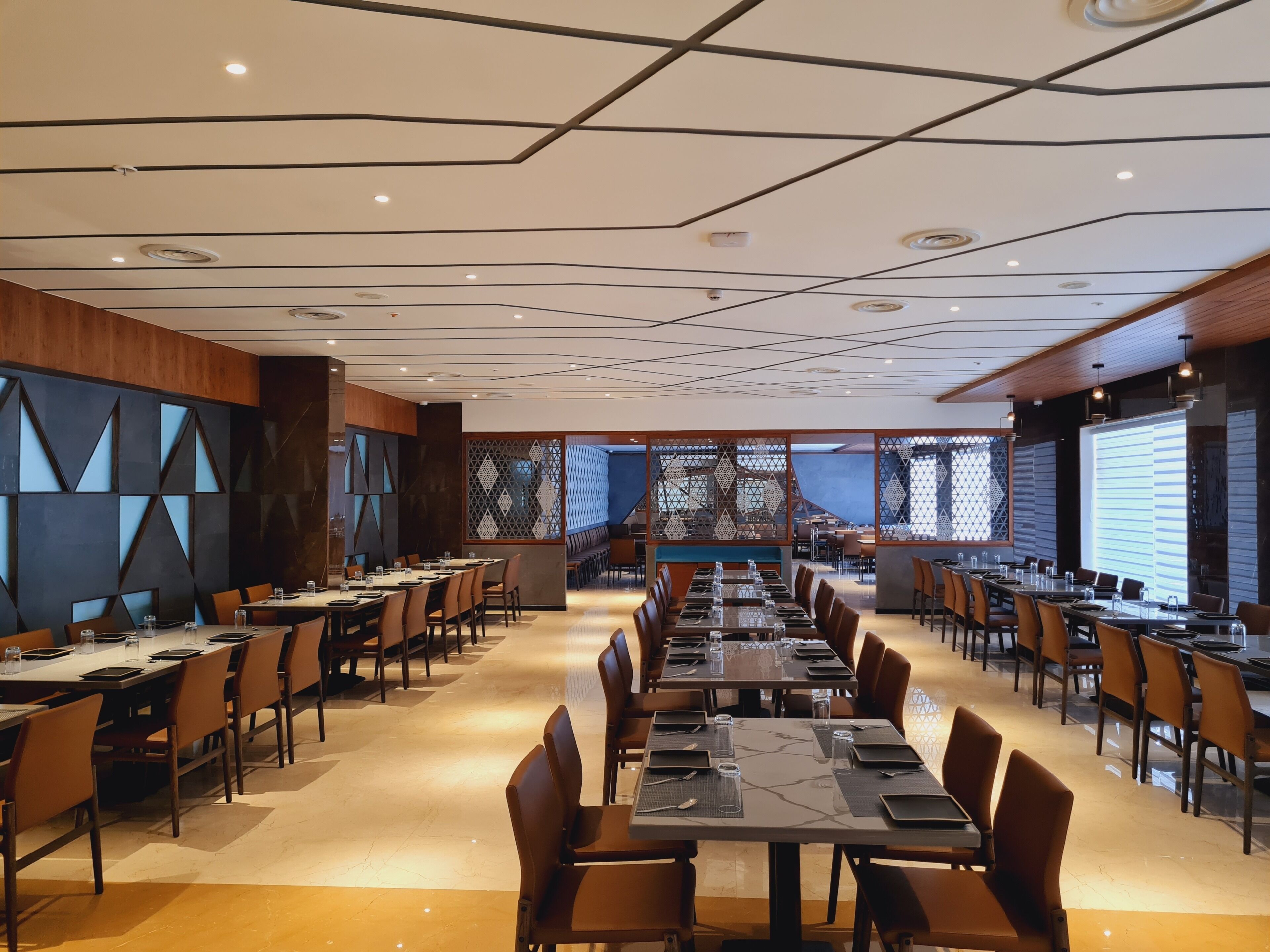 A conference room with multiple tables and chairs, a modern ceiling design, and a view through a patterned partition.