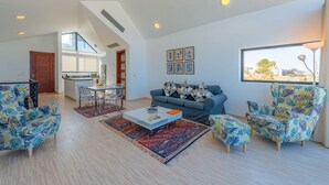 Una sala moderna con un sofá, una mesa de centro y sillones estampados. En el fondo se ve un área de comedor con una mesa y sillas.