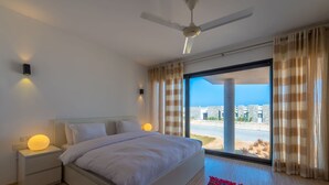 Un dormitorio moderno con una cama grande, un ventilador de techo y vistas de la ciudad a través de ventanales.