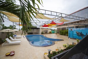An indoor swimming pool with lounge chairs, a mural, and shaded areas. - Koko Maya By Stone Wood (Morjim)
