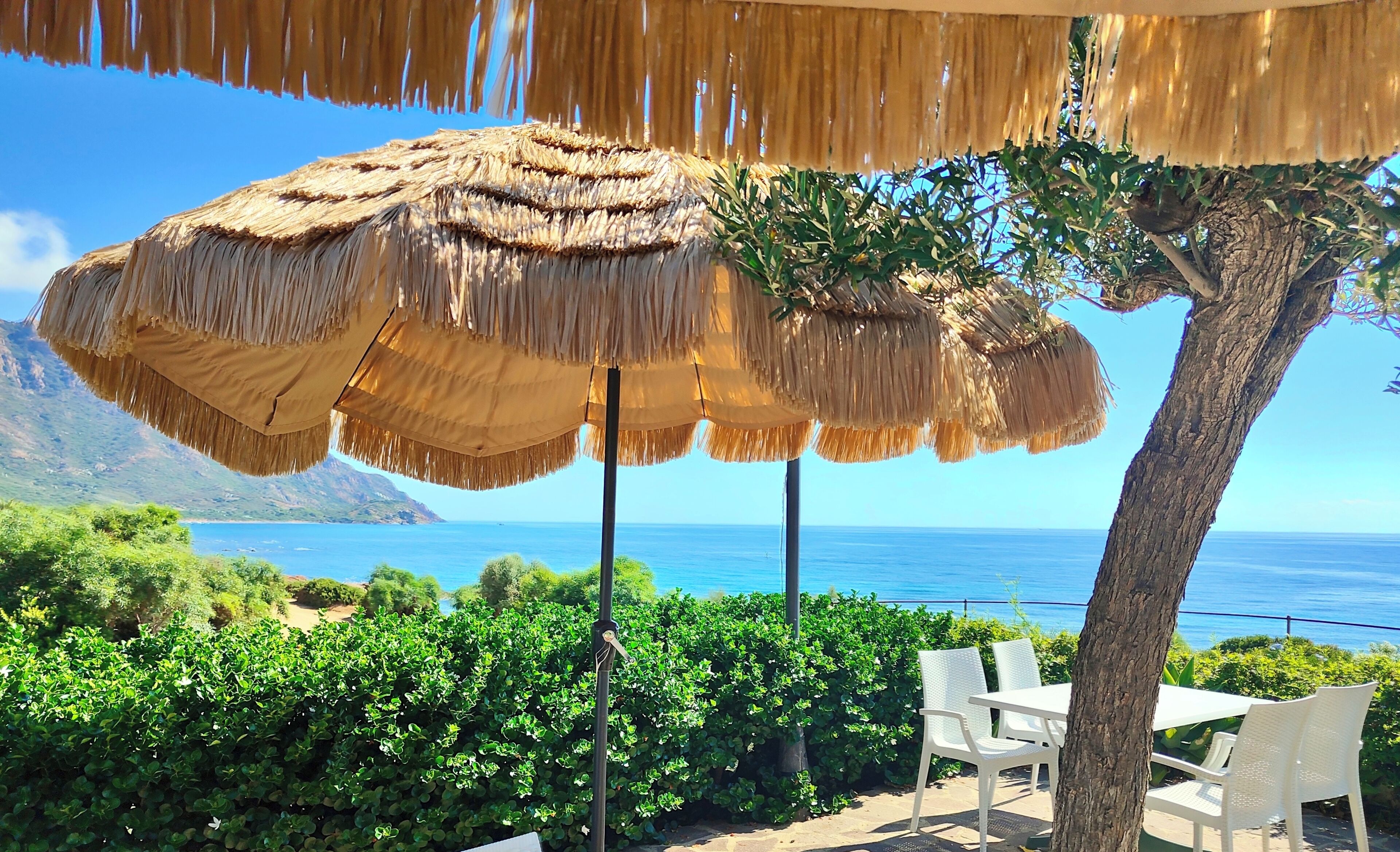 A beachside seating area with thatched umbrellas, white chairs, and a view of the sea.