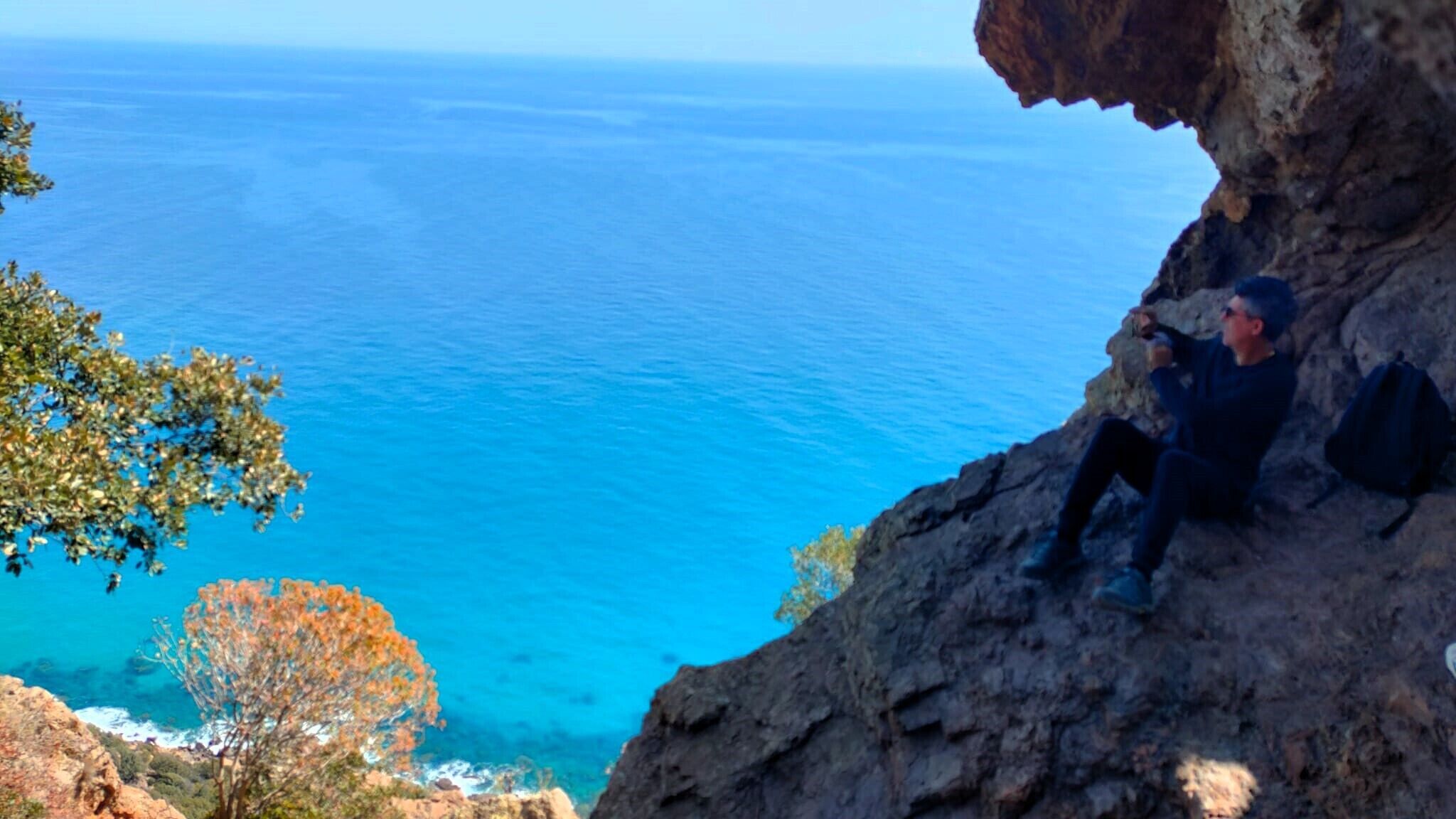 A person sitting on a rocky outcrop overlooking a clear blue sea.