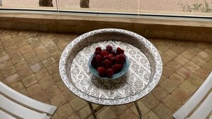 A balcony with a table holding a bowl of strawberries, overlooking a courtyard with palm trees and a building in the background. - La Perla de Marrakech (Marrakech)