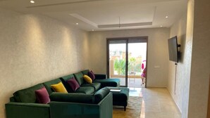 A living room with a sectional sofa, a flat-screen TV mounted on the wall, and a sliding glass door leading to an outdoor area. - La Perla de Marrakech (Marrakech)