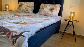 Un dormitorio con una cama tapizada en azul oscuro, ropa de cama con estampado floral y dos lámparas de noche.
