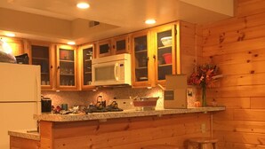 A kitchen with wooden cabinets, a microwave, a refrigerator, and a bar area with stools. - Hear the Waterfalls: Quiet Escape Near Downtown Gatlinburg (Gatlinburg)