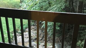 A wooden railing overlooking a rocky stream with dense foliage in the background. - Hear the Waterfalls: Quiet Escape Near Downtown Gatlinburg (Gatlinburg)