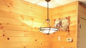 A corner room with wooden walls, a round table with two chairs, a hanging light fixture, and a thermostat on the wall. - Hear the Waterfalls: Quiet Escape Near Downtown Gatlinburg (Gatlinburg)