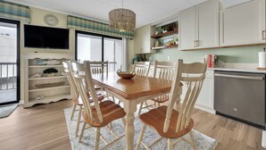 A dining area with a wooden table and chairs, a television above the table, and a kitchen area with cabinets and a dishwasher. - New listing!  Two bedroom, 2 bath with heated pool (Ocean City)