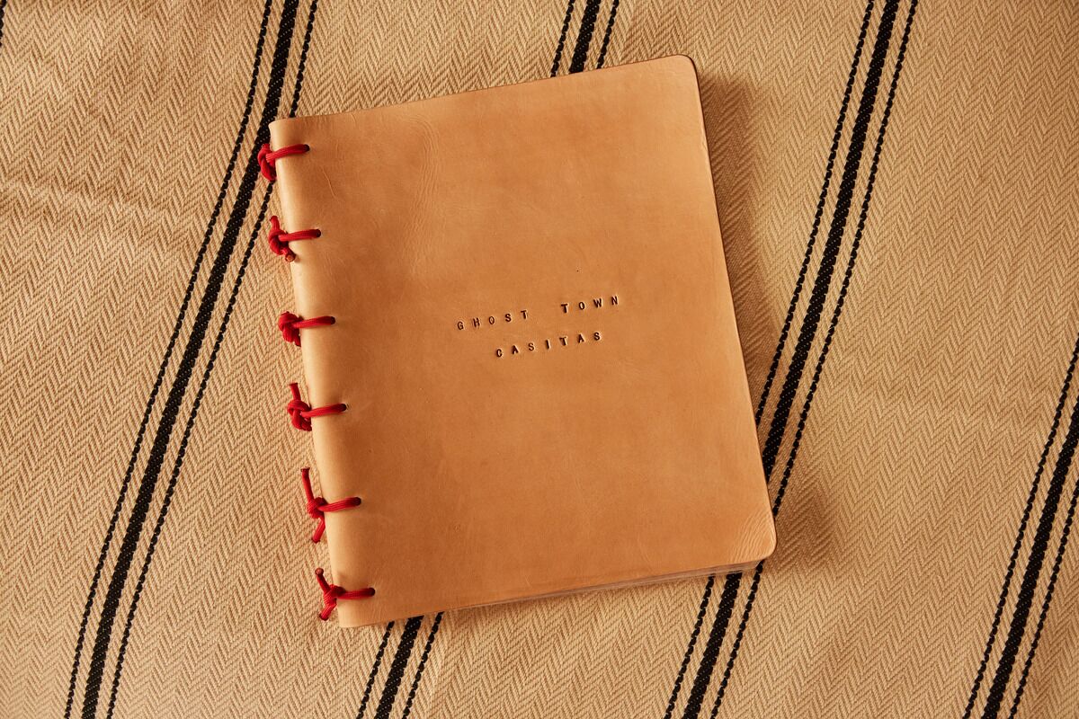 A brown spiral-bound notebook with the text "GHOST TOWN CASITAS" on the cover, placed on a beige fabric with black stripes.