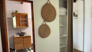 A modern bathroom with a wooden vanity, a mirror, and two woven wall hangings. - Adrien Caraïbes • Domaine de Meilly (Saint-Louis)
