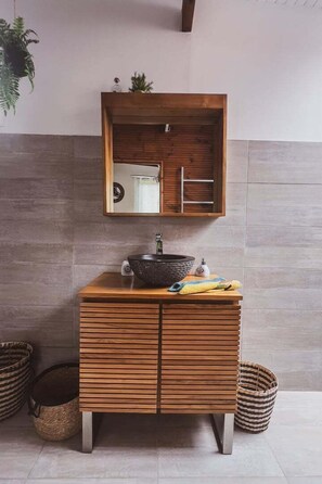 Un baño moderno con tocador de madera, un lavabo redondo, un espejo y dos cestas de mimbre.