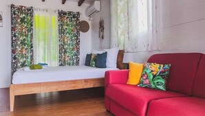 A bedroom with a wooden bed, a red sofa, and tropical-themed curtains. - Adrien Caraïbes • Domaine de Meilly (Saint-Louis)