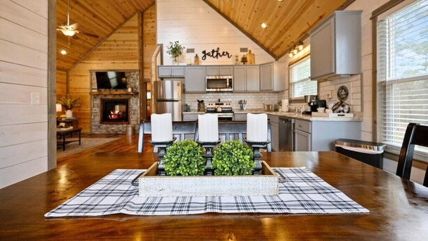 Una cocina acogedora con chimenea, electrodomésticos modernos y un comedor con mantel a cuadros y velas.