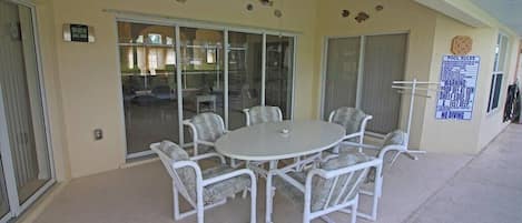 Un espace extérieur abrité avec une table ronde et des chaises, un ventilateur de plafond et un panneau indiquant les rÚgles de la piscine.