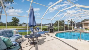 A covered outdoor area with a pool, lounge chairs, and a barbecue grill.