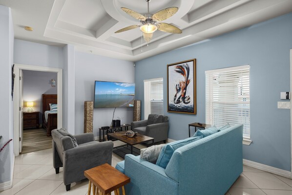 A living room with a ceiling fan, a flat-screen TV, a sofa, and a coffee table. - Sea Glass #10 | Coastal Condo • Community Pool • 3 Min Walk to Beach (South Padre Island)