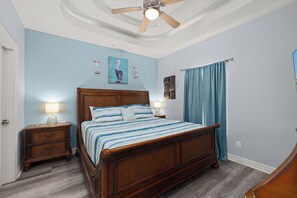 Une chambre à coucher avec un lit en bois, deux tables de chevet avec des lampes, un ventilateur de plafond et un luminaire fixé au mur.