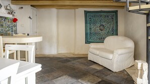 A room with a stone floor, a white chair, a small table, and a tapestry on the wall.