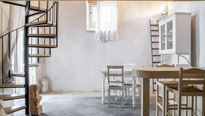 A room with a spiral staircase, a dining table with chairs, a cabinet, and a window with curtains.