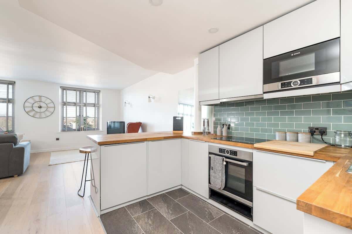 Een moderne keuken met witte kastjes, een Bosch magnetron en een betegelde spatwand.