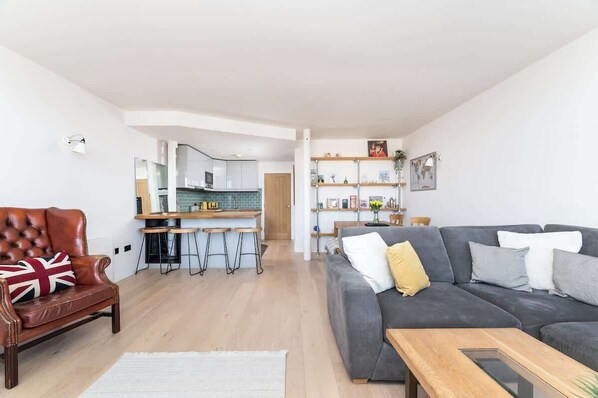 Una sala de estar moderna con un sofá, un sillón de cuero y un comedor con taburetes.