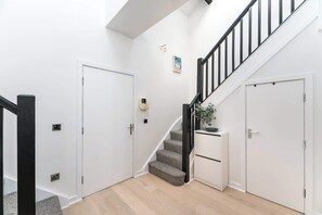 Una escalera con barandilla negra, paredes blancas y piso cubierto de alfombra gris.