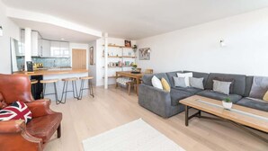 A modern living room with a grey sofa, a wooden coffee table, a leather armchair, and a kitchen in the background. - Free Secure Parking | Stunning City Views (York)