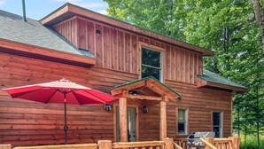 Une cabane en bois avec une véranda, un parasol rouge et un barbecue.