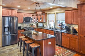 A modern kitchen with wooden cabinets, stainless steel appliances, and a central island with stools. - Trails End House in Inlet (Inlet)