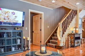 A wooden staircase with a railing, a television mounted on the wall, and a glass table with a candle. - Trails End House in Inlet (Inlet)
