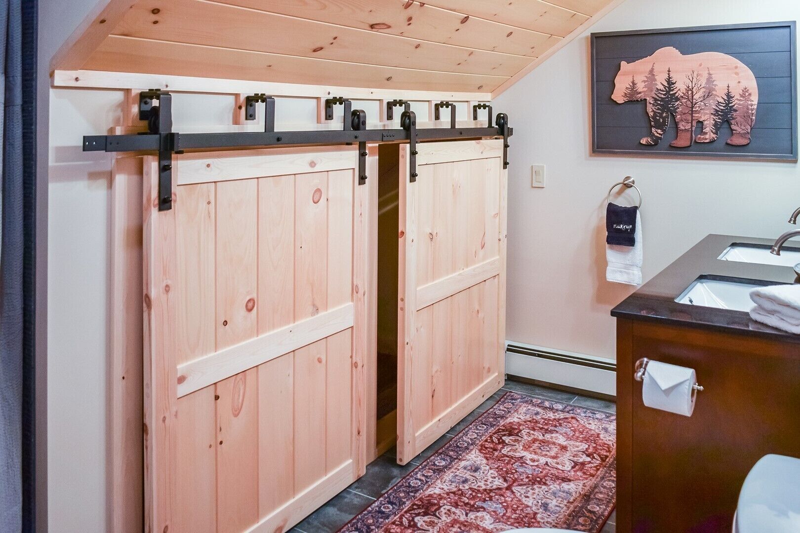 A bathroom with a wooden sliding door closet, a sink with a dark countertop, and a bear-themed wall decoration.