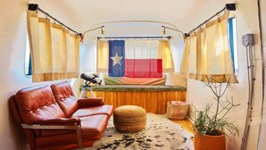 A cozy interior with a leather sofa, a small round ottoman, a Texas flag, and a potted plant. - Air Conditioned Escape ⁠— Quick Drive from Big Ben (Terlingua)