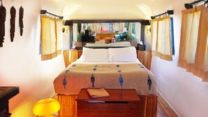 A bedroom with a bed, a nightstand, a lamp, and a view of a room through a window. - Air Conditioned Escape ⁠— Quick Drive from Big Ben (Terlingua)