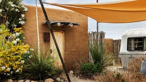 A rustic building with a wooden door, surrounded by desert flora and a parked RV. - Air Conditioned Escape ⁠— Quick Drive from Big Ben (Terlingua)