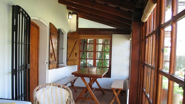 A covered patio with a wooden table and chairs, a wicker chair, and a white sofa. - 2 bedroom apartment, Roche (Roche)