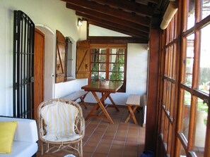 A covered patio with a wooden table and chairs, a wicker chair, and a white sofa. - 2 bedroom apartment, Roche (Roche)