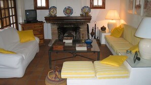 A living room with a fireplace, a sofa, a striped couch, a coffee table, and a television. - 2 bedroom apartment, Roche (Roche)