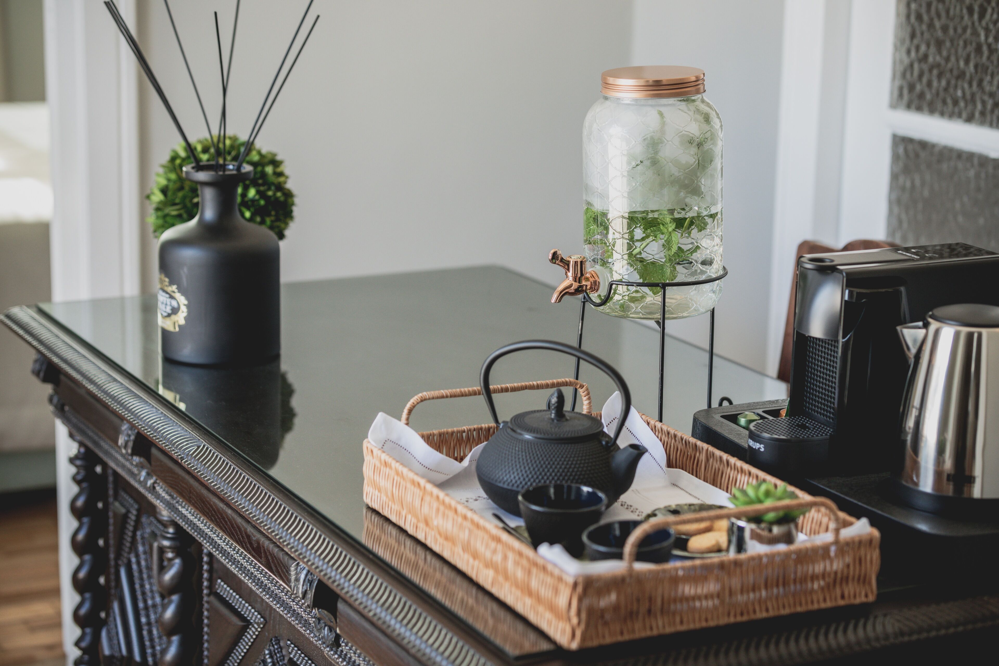 Una mesa de madera con un juego de té, un tarro de cristal con tapa de cobre y un hervidor negro.