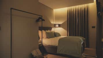 Quarto de hotel com cama, mesa de cabeceira, abajur e cortina.