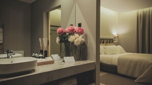 A hotel bathroom with a large mirror, a sink, and a vanity with toiletries. There are two vases with flowers on the vanity. - Casal dos Capelinhos - Quinta Nova (Santa Marta de Penaguião)